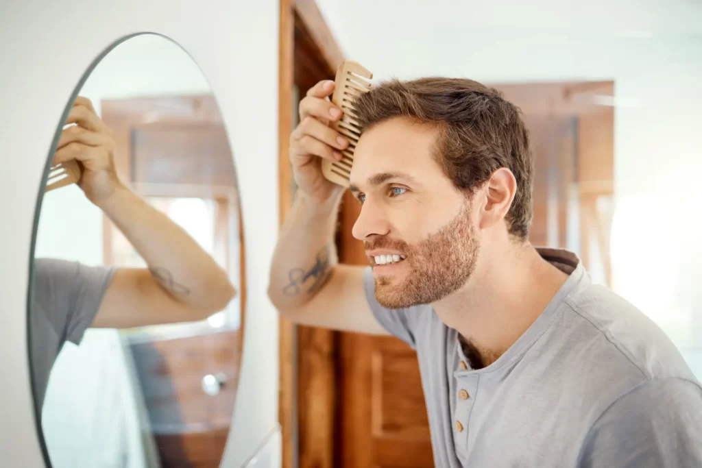 man combs hair looking in bathroom mirror utc